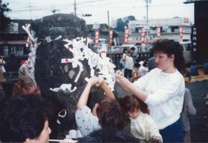 Family putting O-mikuji (prayer papers) on a rock during a celebration in Oita