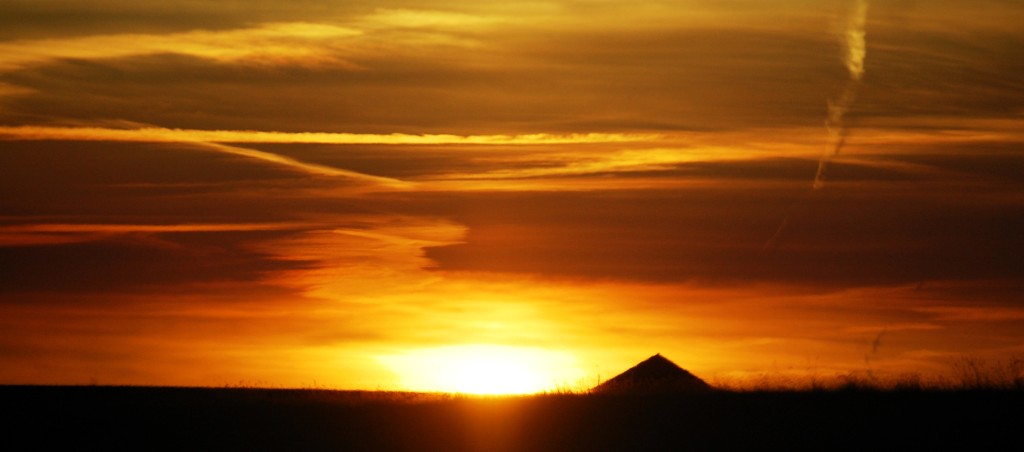 The roof of a barn is silhouetted in the sunset east of Glasgow, MT on US Route 2 